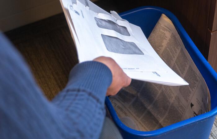 A person putting mail and a newspaper in a recycling bin.